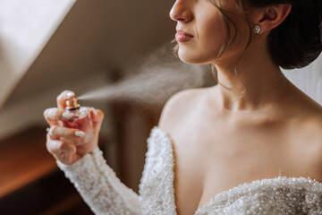 The brunette bride, holds perfume in her hands, wants to apply it on herself. Voluminous veil....