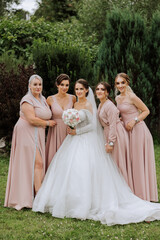 Fototapeta na wymiar A brunette bride and her bridesmaids in identical pink dresses are standing against the background of nature. Girls in identical dresses are making out at a wedding. Wedding in nature.
