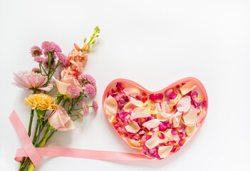 Bouquet of fresh flowers with roses, carnations and chrysanthemums with pink ribbon in shape of heart filled with rose petals. Romantic greetings on Valentine's Day, March 8 or Birthday