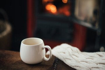 White cup with tea with burning fireplace on the background in cozy log cabin.