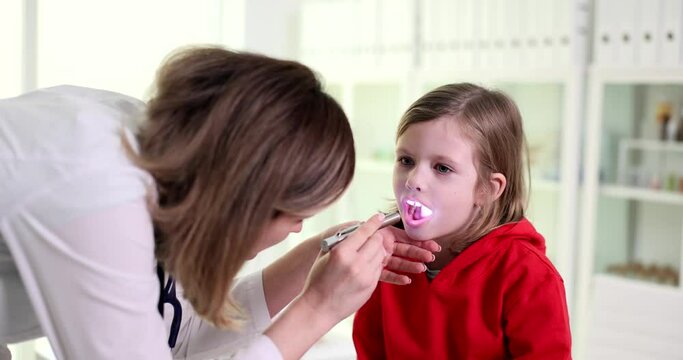 Female otolaryngologist doctor shines light into throat of patient child with pain syndromes. Enlarged tonsils in child and acute tonsillitis