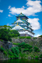 Naklejka premium Osaka Castle in Daylight: Majestic Fortress Amidst Vibrant Sky and Tranquil Waters