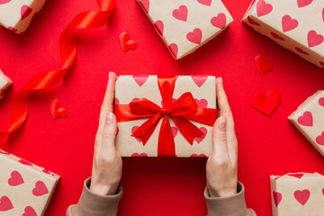 Give a gift on Valentine Day.Valentine gift. Beauty Woman hands holding Gift box with red bow over...
