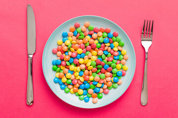 cutlery on table and sweet plate of candy. Health and obesity concept, top view on colored background