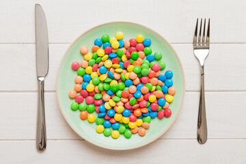 cutlery on table and sweet plate of candy. Health and obesity concept, top view on colored background