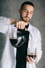 Handsome barista pouring freshly brewed drip coffee in a glass mug. Preparing coffee alternative method.