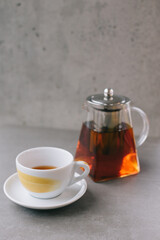 Glass teapot and cup with aromatic tea isolated on gray background.