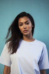Fototapeta premium Young pretty cool Indian woman model wearing tshirt looking at camera standing on color background. Face skin care cosmetics makeup, fashion ads. Beauty portrait. White t-shirt mock up template .