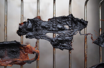 Burnt and overcooked meat, bacon rashers on a barbecue grill.