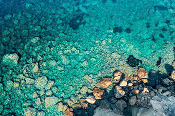 Aerial top down view of Cyprus ocean azure water surface, showcasing rocks amidst crashing waves below © DedMityay