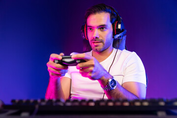 Smart gaming streamer concentrating gaming players trying to pass the level at mission completed with joystick control, talking others via mic on streaming live at neon lighting studio room. Surmise.