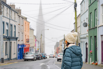 Woman with wool hat walking while enjoying the streets of a picturesque town in Ireland on her car trip through the country