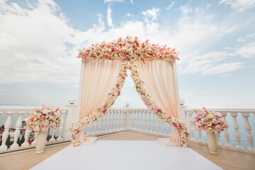 Wedding arch peach color with flowers on the background of the sea. Vases with fresh flowers.