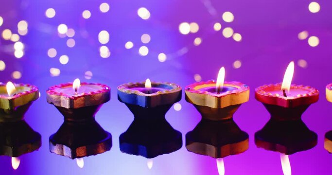 Close up of lights and burning candles celebrating diwali on purple background, with copy space