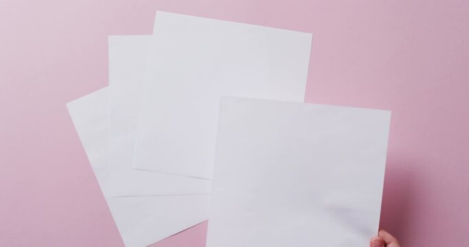 Hand holding piece of paper over pieces of paper with copy space on pink background in slow motion