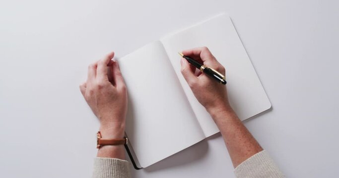 Close up of hand writing with pen on book with copy space on white background in slow motion