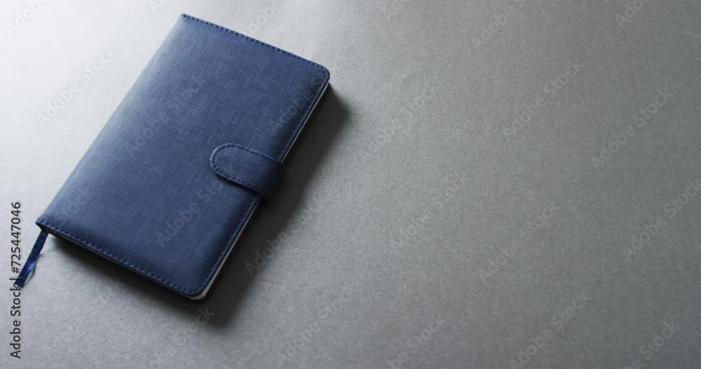Poster close up of closed blue notebook with copy space on gray background in slow motion