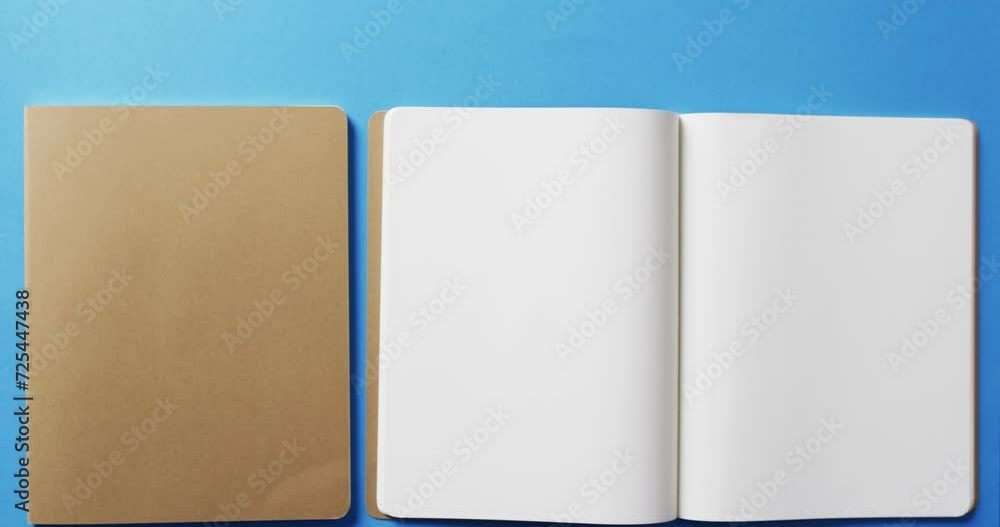 Poster close up of open blank book and brown notebook with copy space on blue background in slow motion