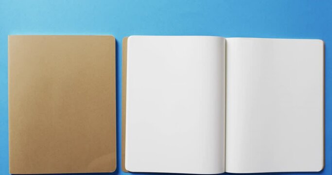 Close up of open blank book and brown notebook with copy space on blue background in slow motion