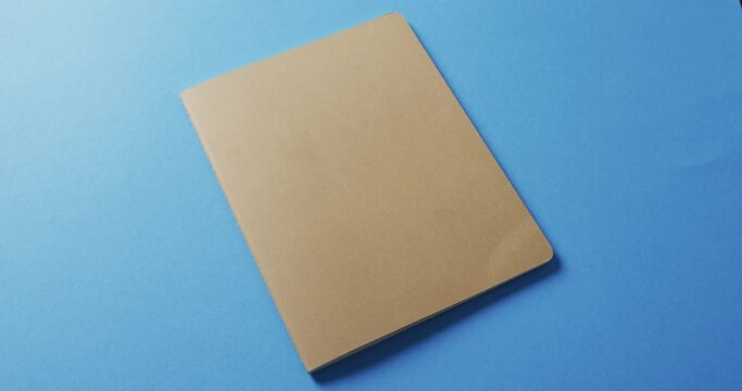 Close up of closed brown book with copy space on blue background in slow motion