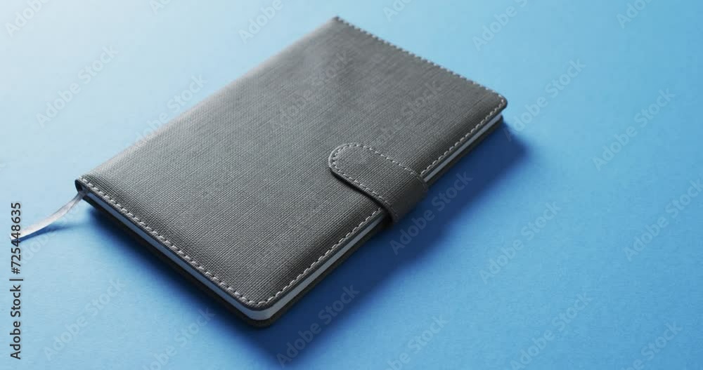 Poster close up of closed gray notebook with copy space on blue background in slow motion