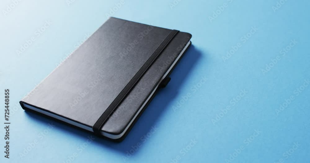 Poster close up of closed black notebook with copy space on blue background in slow motion