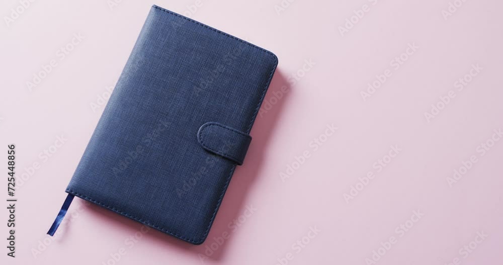 Poster close up of closed blue notebook with copy space on pink background in slow motion