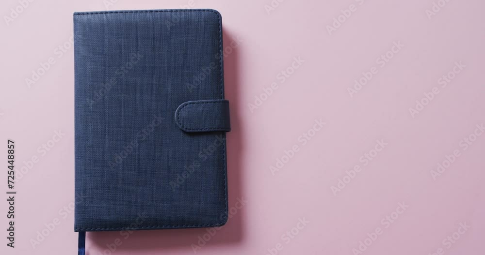 Poster close up of closed blue notebook with copy space on pink background in slow motion