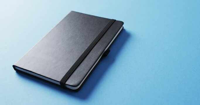 Close up of closed black notebook with copy space on blue background in slow motion