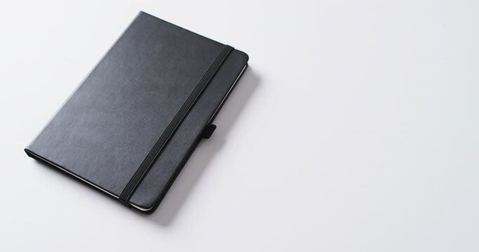 Close up of closed black notebook with copy space on white background in slow motion