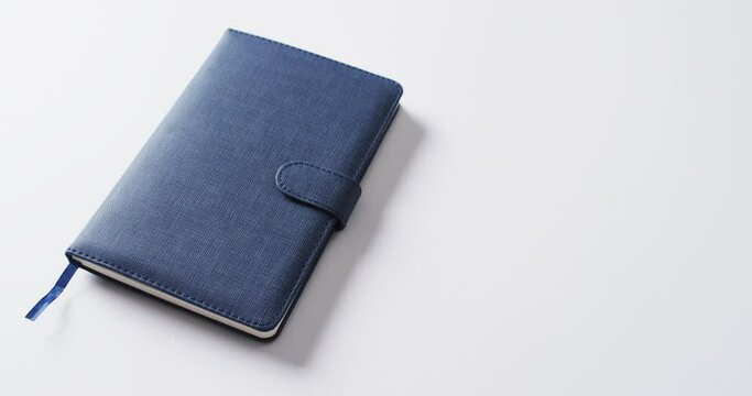 Close up of closed blue notebook with copy space on white background in slow motion