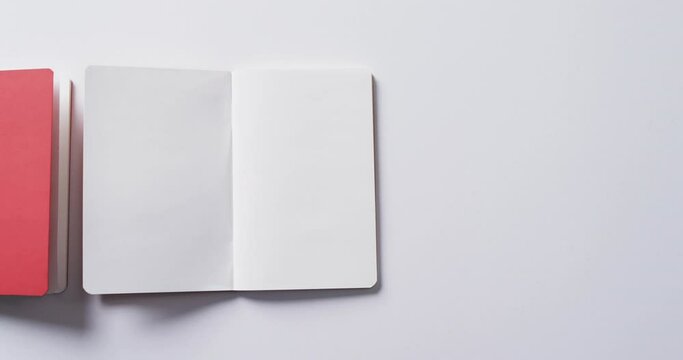 Close up of closed red book and open blank book with copy space on white background in slow motion