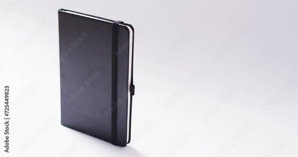 Poster closed black notebook standing vertical with copy space on white background in slow motion