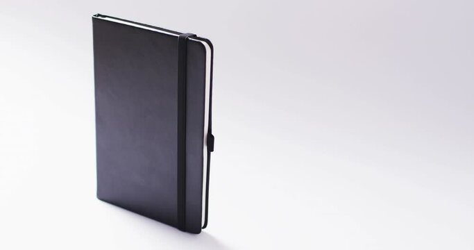 Closed black notebook standing vertical with copy space on white background in slow motion