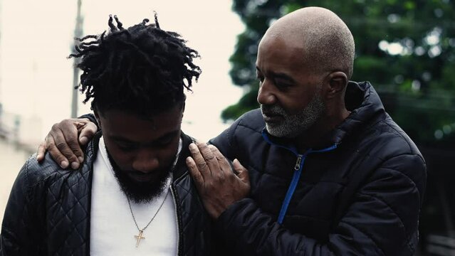 African American Father Mentoring Adult Son, Hand on Shoulder in Urban Street, Authentic family lifestyle of attentive 50s parent orienting young man