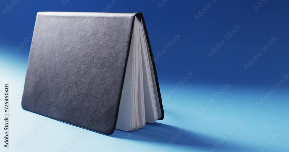 Poster close up of open black book standing horizontal with copy space on blue background in slow motion