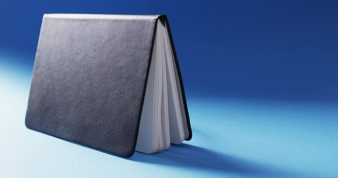 Close up of open black book standing horizontal with copy space on blue background in slow motion