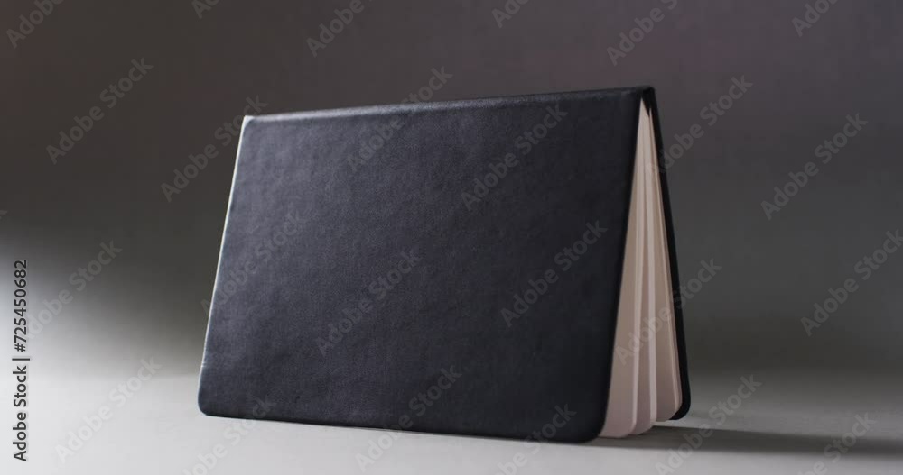 Poster close up of open black book standing horizontal with copy space on gray background in slow motion