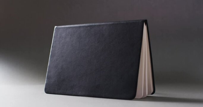 Close up of open black book standing horizontal with copy space on gray background in slow motion
