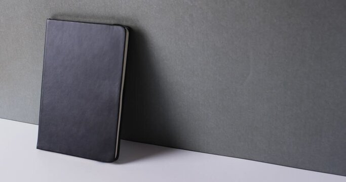 Close up of closed black book leaning on wall with copy space on gray background in slow motion