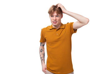 smart young red-haired caucasian male student with a tattoo dressed in a mustard t-shirt is holding his head
