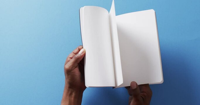Close up of hand leafing through book with copy space on blue background in slow motion