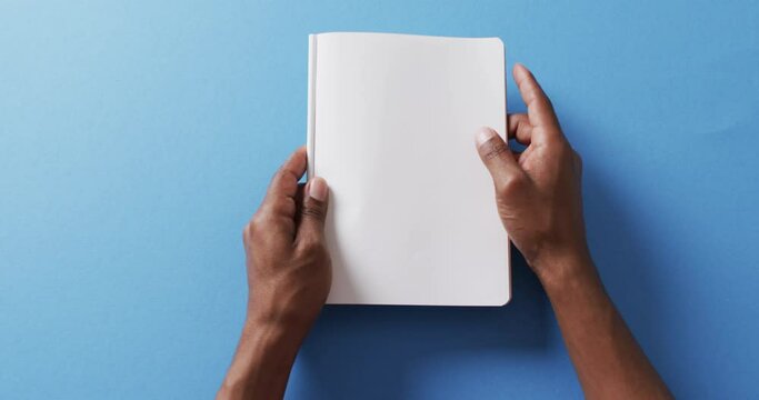 Close up of hand leafing through book with copy space on blue background in slow motion