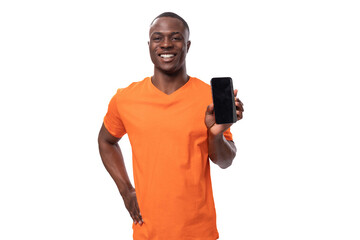 young american man in orange t-shirt holding smartphone screen forward with mockup