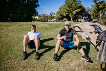 Sotogrante, Spain - January 25, 2024 - Two men are sitting on the grass at a golf course, resting, with a golf bag and clubs beside them.