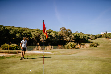 Sotogrante, Spain - January 25, 2024 - A golfer stands on the green near the hole with a flagstick, in a sunny golf course setting.