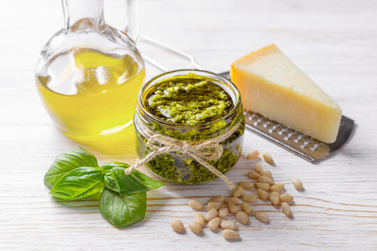 Homemade pesto sauce in small glass jar and ingredients for pasta on white wooden background with copy space. Traditional Italian cuisine, recipe, restaurant menu