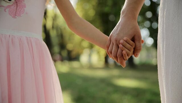 Mother and child holding hands on sunset background. Daughter takes mother's hand in park. Sun flares nature. Concept of family, trust, love and happiness