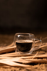 Transparent cup with coffee on the sand among palm leaves