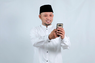 Happy asian muslim man holding and pointing on phone cellular over white background. Ramadan concept